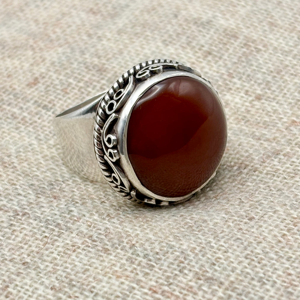 Front view of a polished oval carnelian statement ring in sterling silver, showing deep red-orange stone tones and ornate carved setting