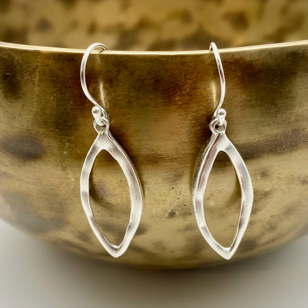 Handmade sterling silver open marquise drop earrings resting against a warm ceramic bowl, showing scale and satin-matte surface finish