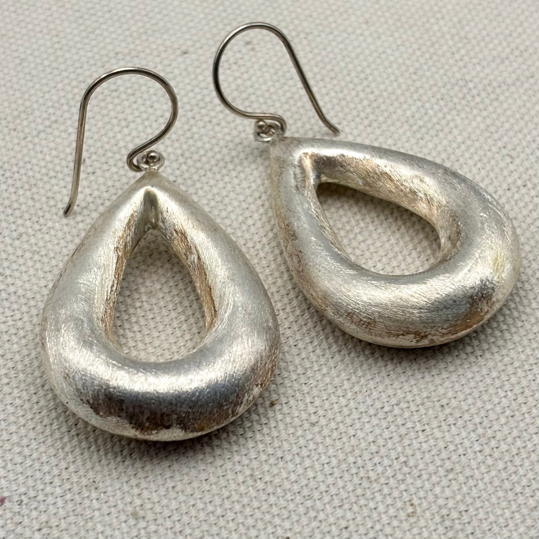 Angled view of large handmade sterling silver teardrop earrings showing brushed surface finish and depth of form