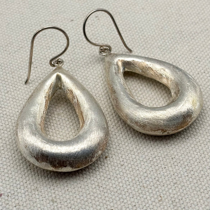 Angled view of large handmade sterling silver teardrop earrings showing brushed surface finish and depth of form