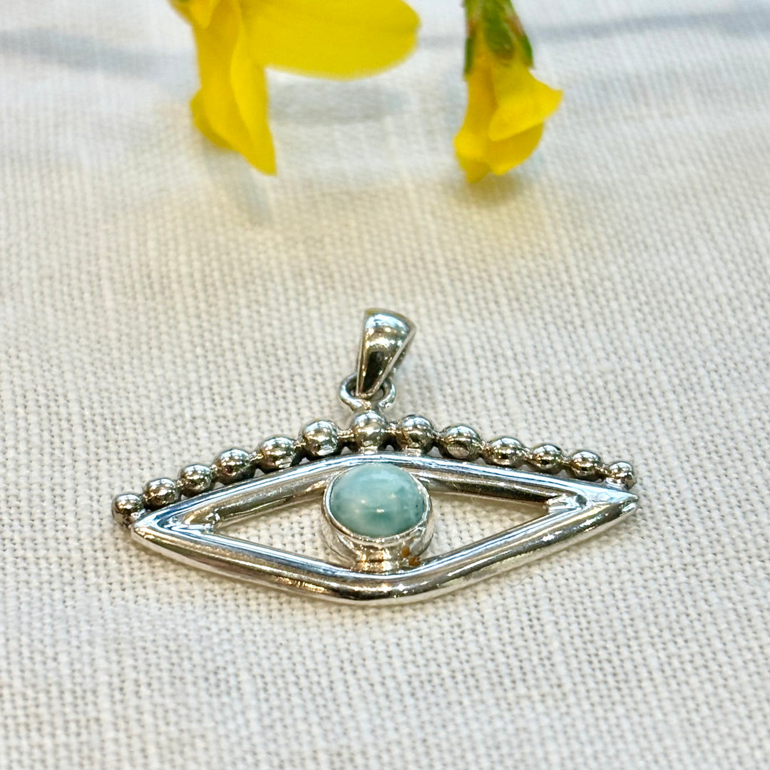 Handmade sterling silver larimar evil eye pendant necklace styled with yellow flowers, showing pendant detail and chain