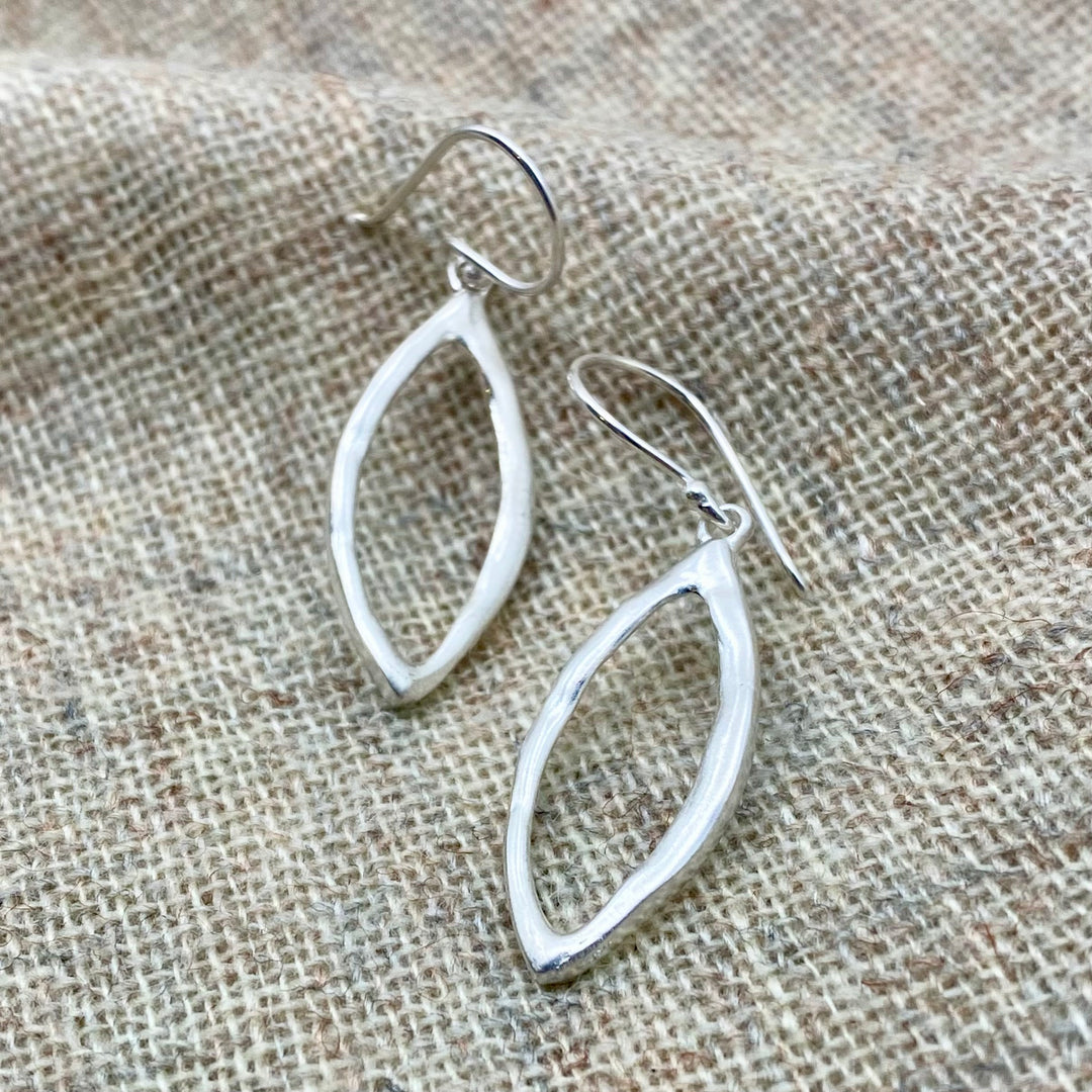 Handmade sterling silver marquise drop earrings with open leaf shape and satin-matte finish, photographed on textured fabric background