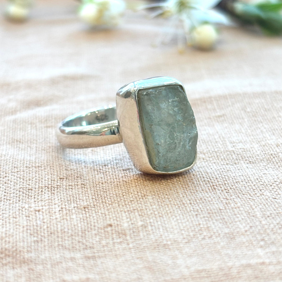 Close-up of a rectangular raw grey moonstone in a sterling silver bezel setting, showing natural surface texture and pale tonal variations
