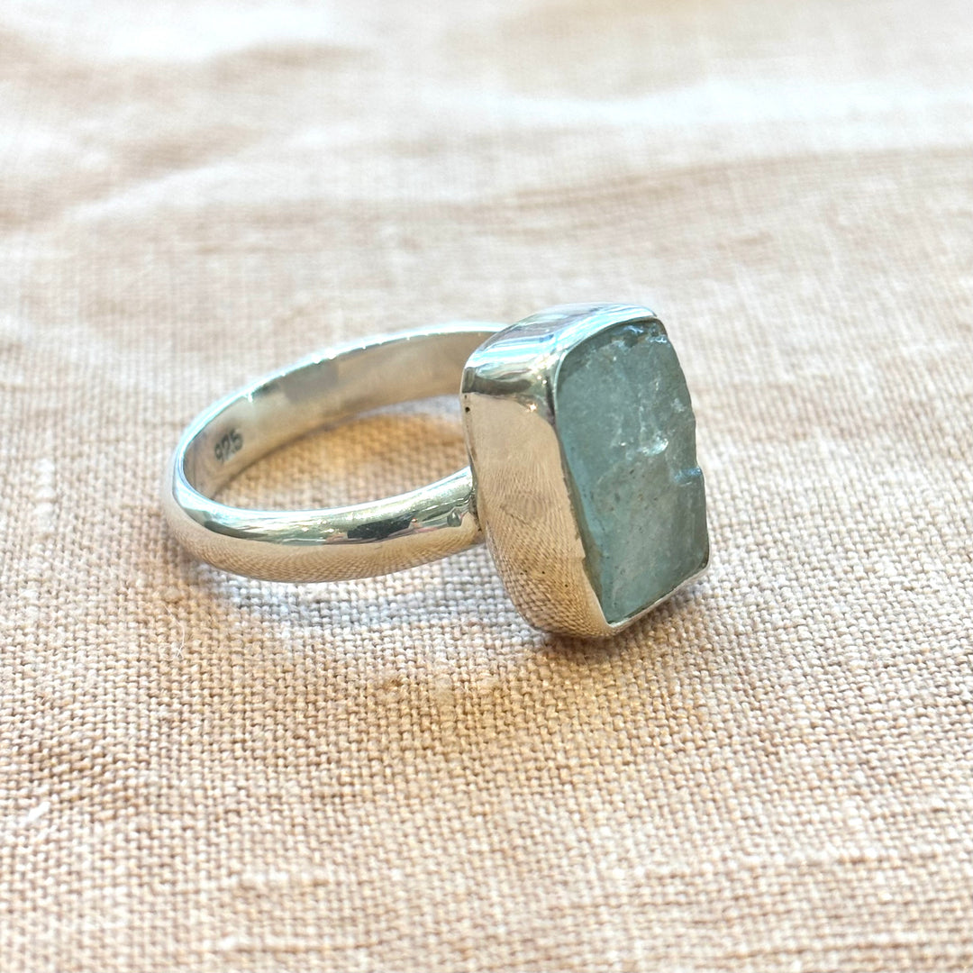 Side view of a handmade sterling silver bezel ring with a rectangular raw grey moonstone, showing polished band profile