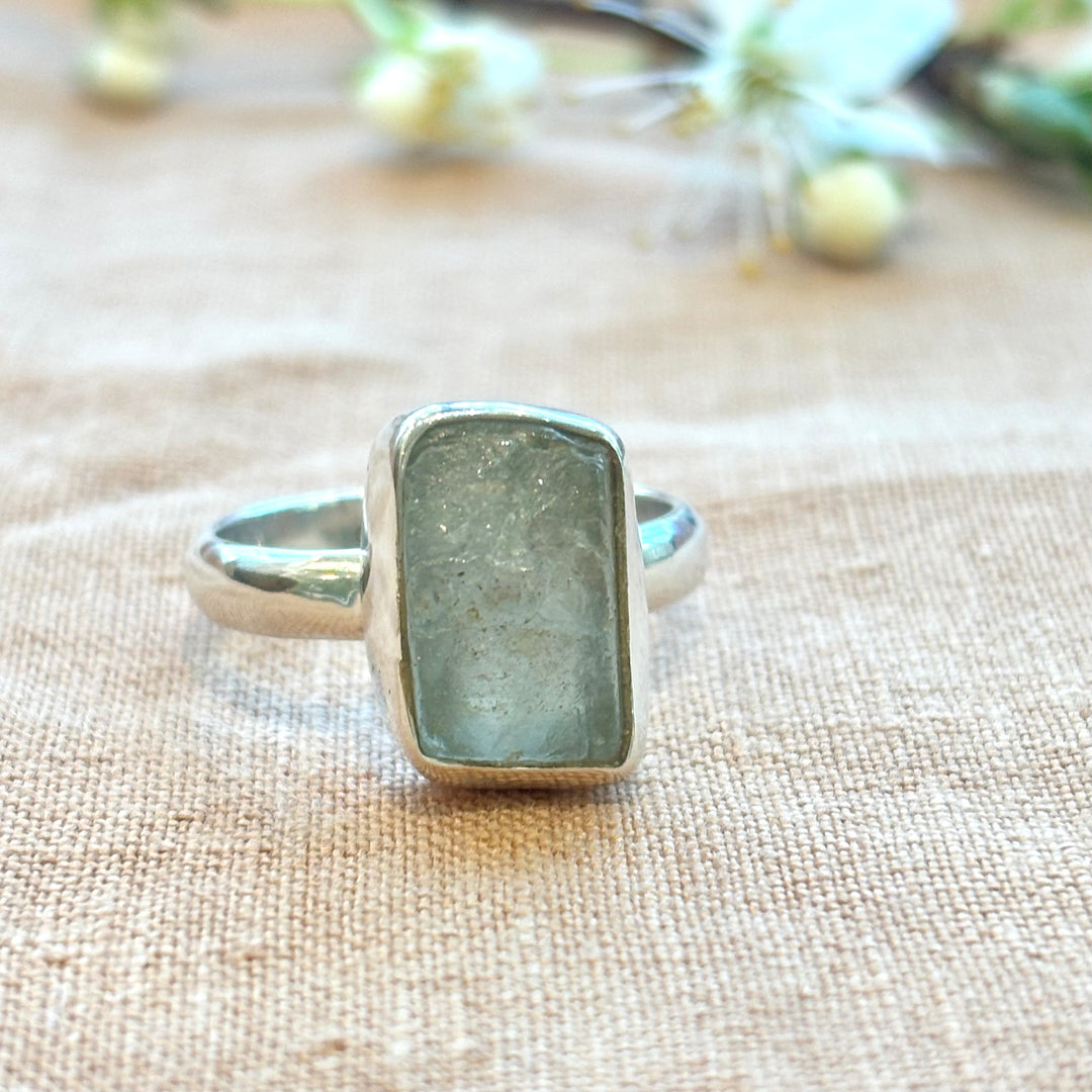 Raw grey moonstone set in a handmade sterling silver bezel ring, photographed on a natural linen background