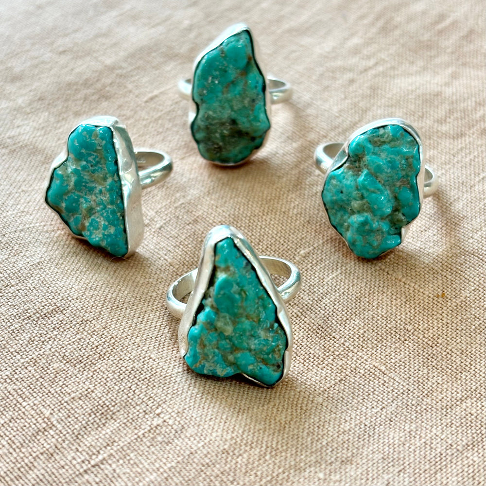 Four raw turquoise sterling silver rings arranged together showing natural variation in stone colour and matrix pattern between each piece